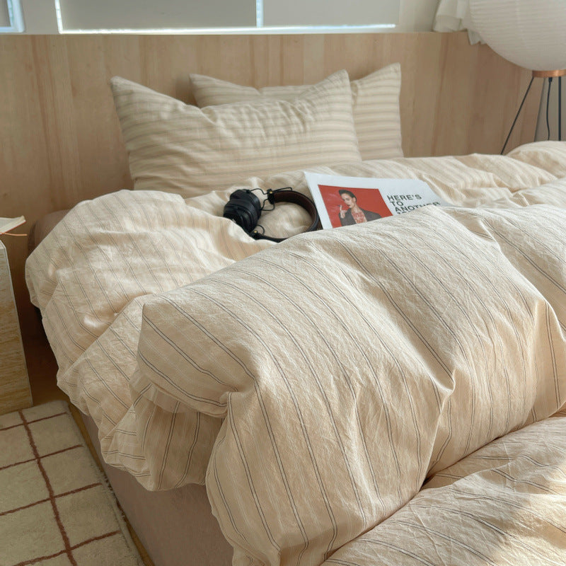 Beige striped bedding on a bed with a cat and a book in a cozy bedroom.