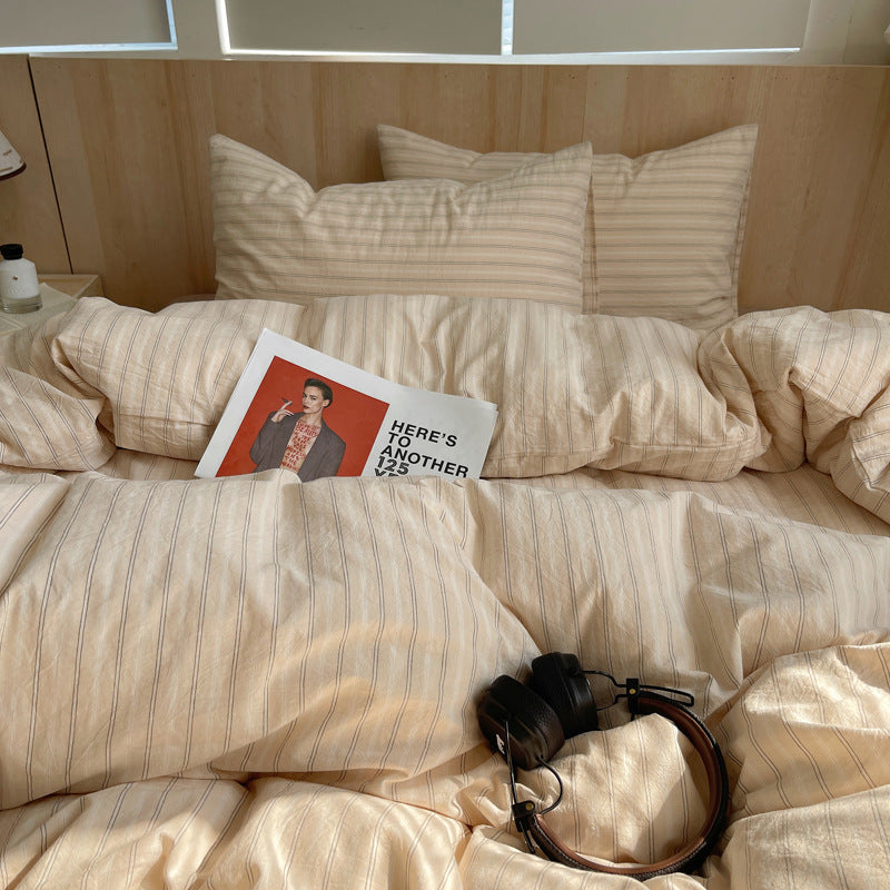 Beige striped bed with a magazine and headphones on top, wooden headboard in the background