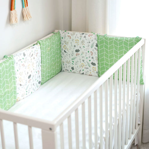 White crib with green and white patterned bumper pads in a room.