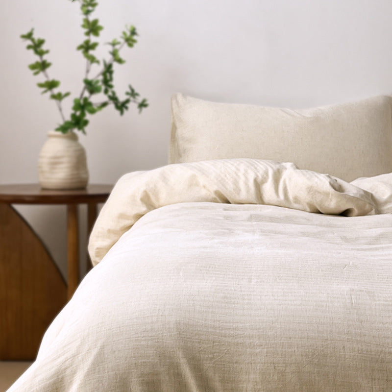 Beige bedding on a bed with a side table and plant in the background